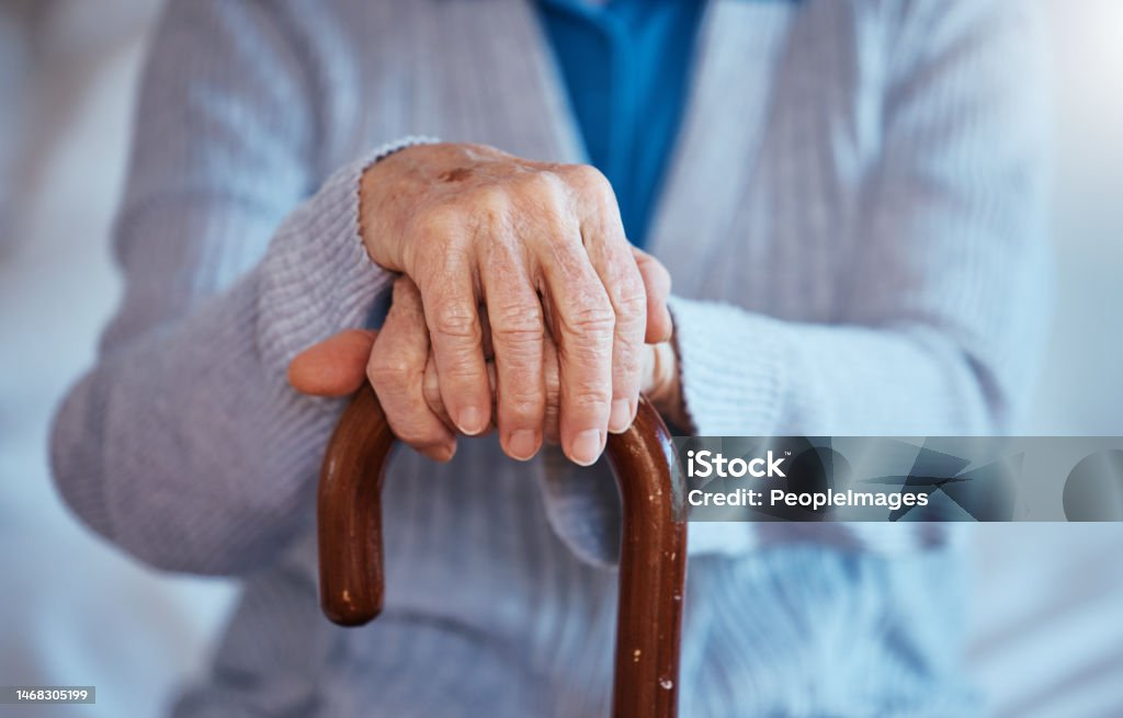 An elderly person's hands resting on a walking cane